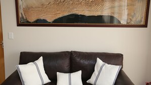 A framed topographic map on a wall above a brown leather sofa with three white pillows. - Stay at Swakop Guesthouse (Swakopmund)