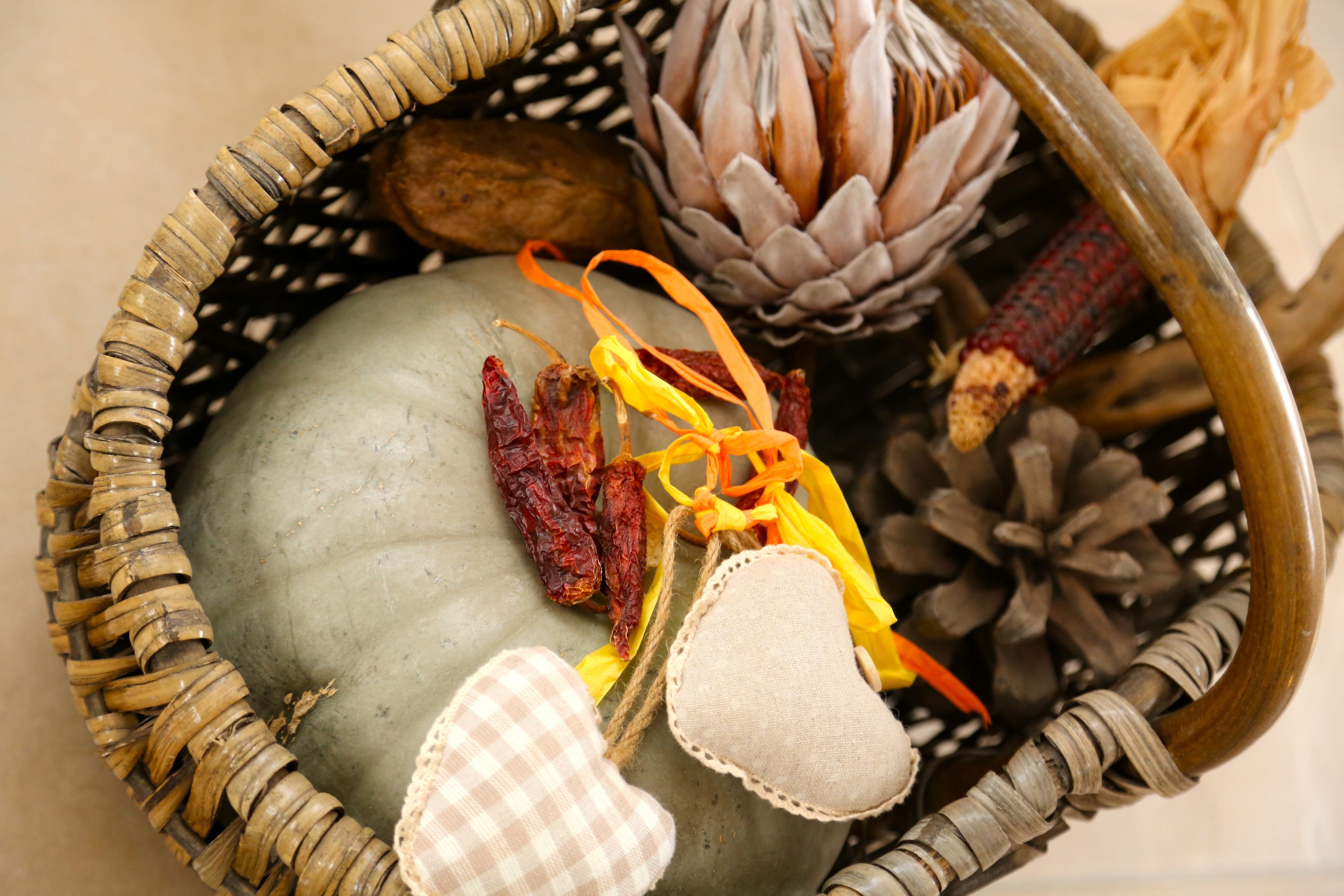 Un panier en osier contenant des fleurs séchées, une pomme de pin et un objet en tissu en forme de cœur.