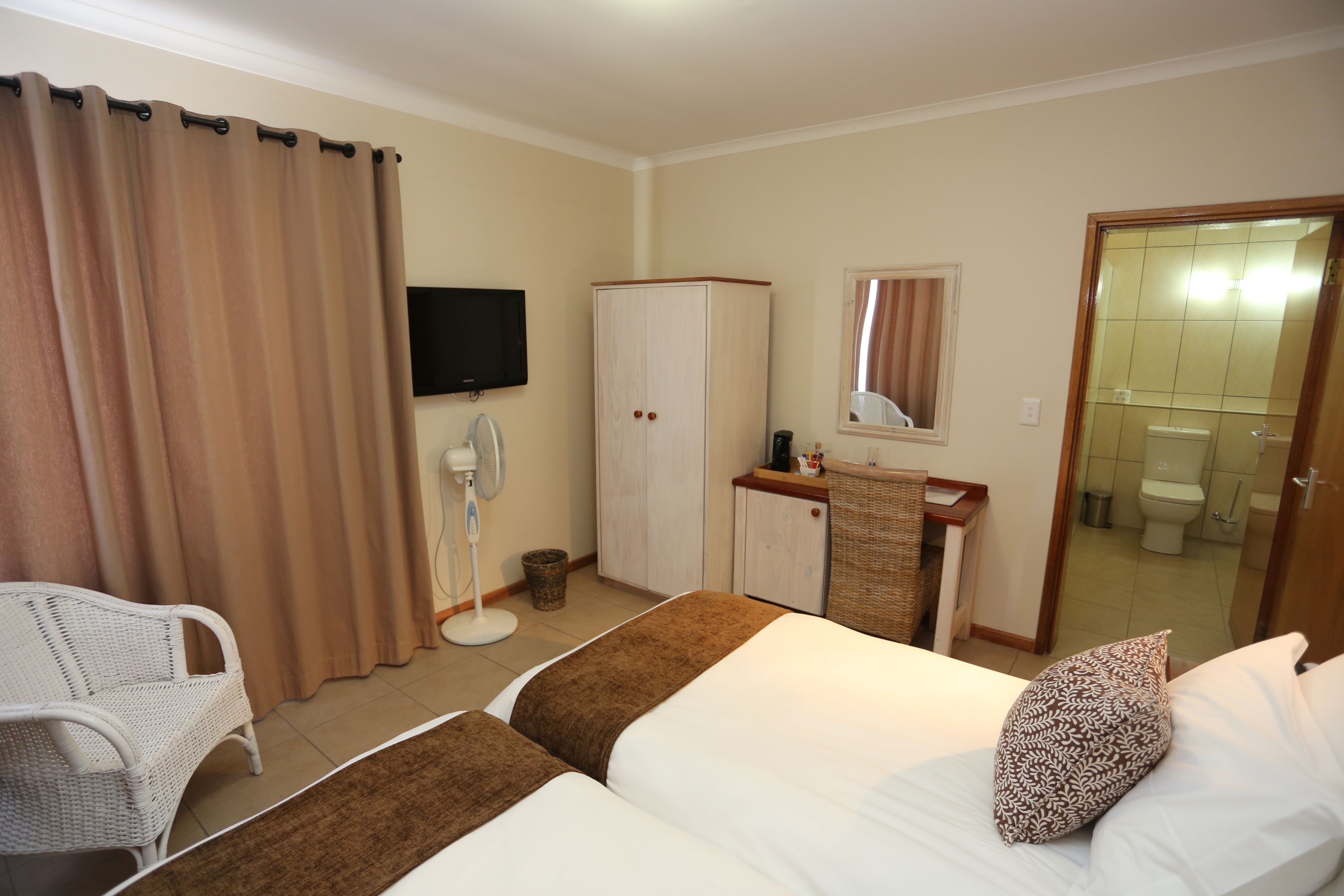 A hotel room with two beds, a desk, a television, a wardrobe, and a bathroom visible through an open door.