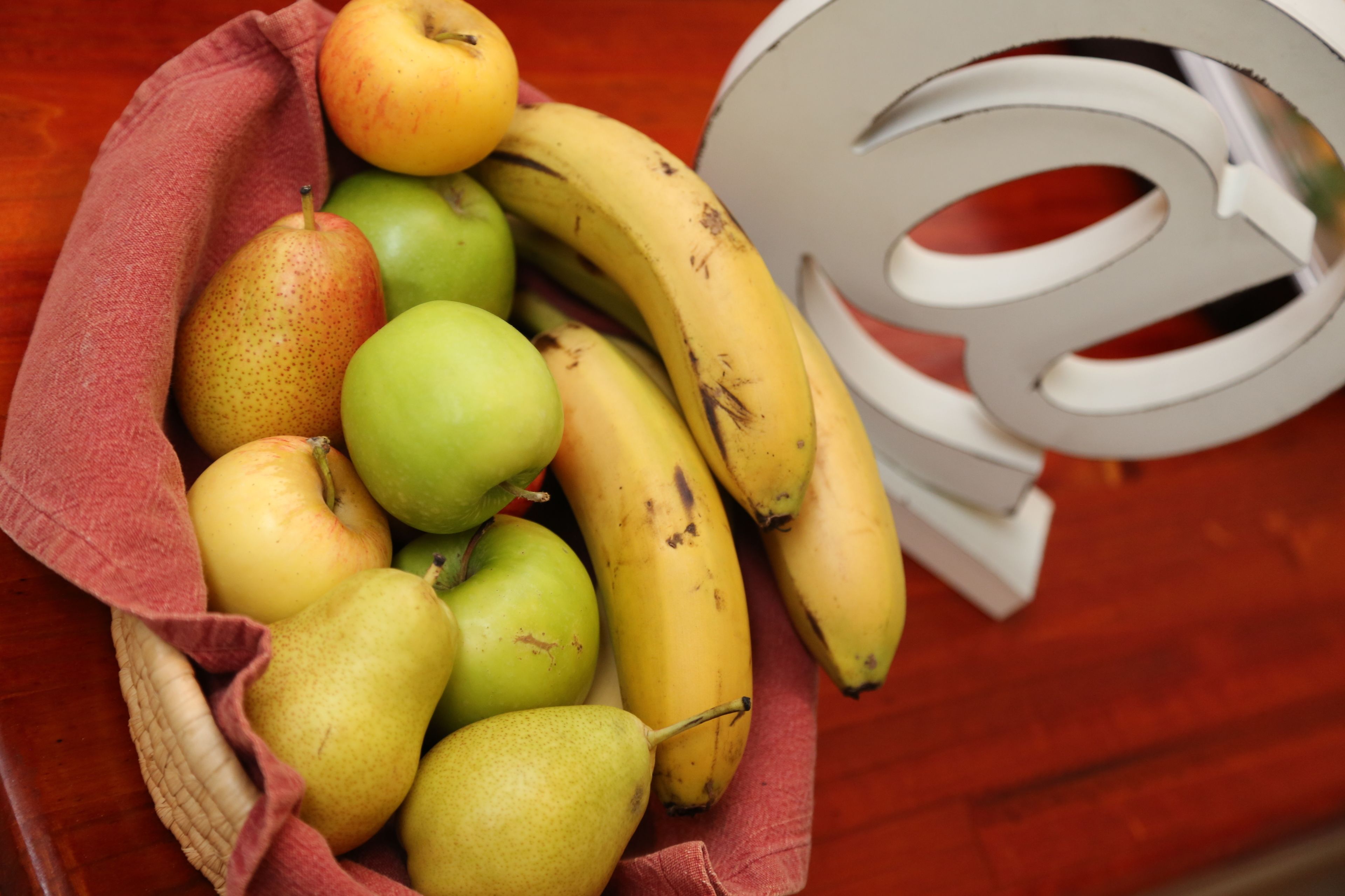 Een mand met fruit, waaronder bananen en peren, op een houten ondergrond.