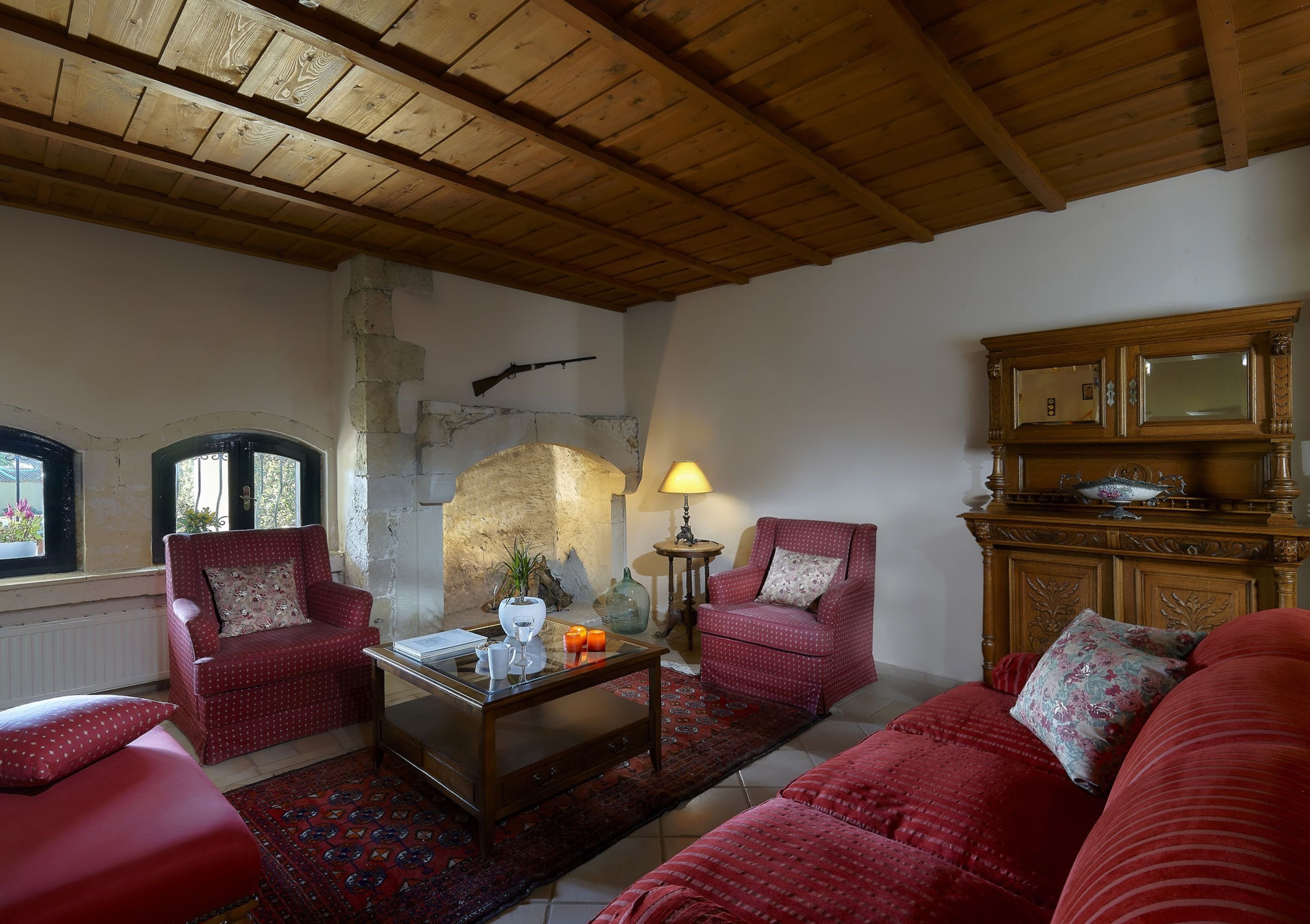 A cozy living room with a fireplace, two red armchairs, a wooden coffee table, and a red sofa.