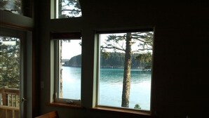 A bedroom with a bed, two windows, and a view of a lake and trees. - Kodiak Awesome View Vacation Rentals: The  Captains Quarters (Kodiak)