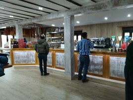 Um café com balcão de madeira e máquina de café. Há pessoas em pé no balcão.