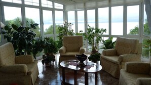 A sunlit room with large windows, a round coffee table, and two armchairs. - Pensión El Carloto (Campoo de Yuso)