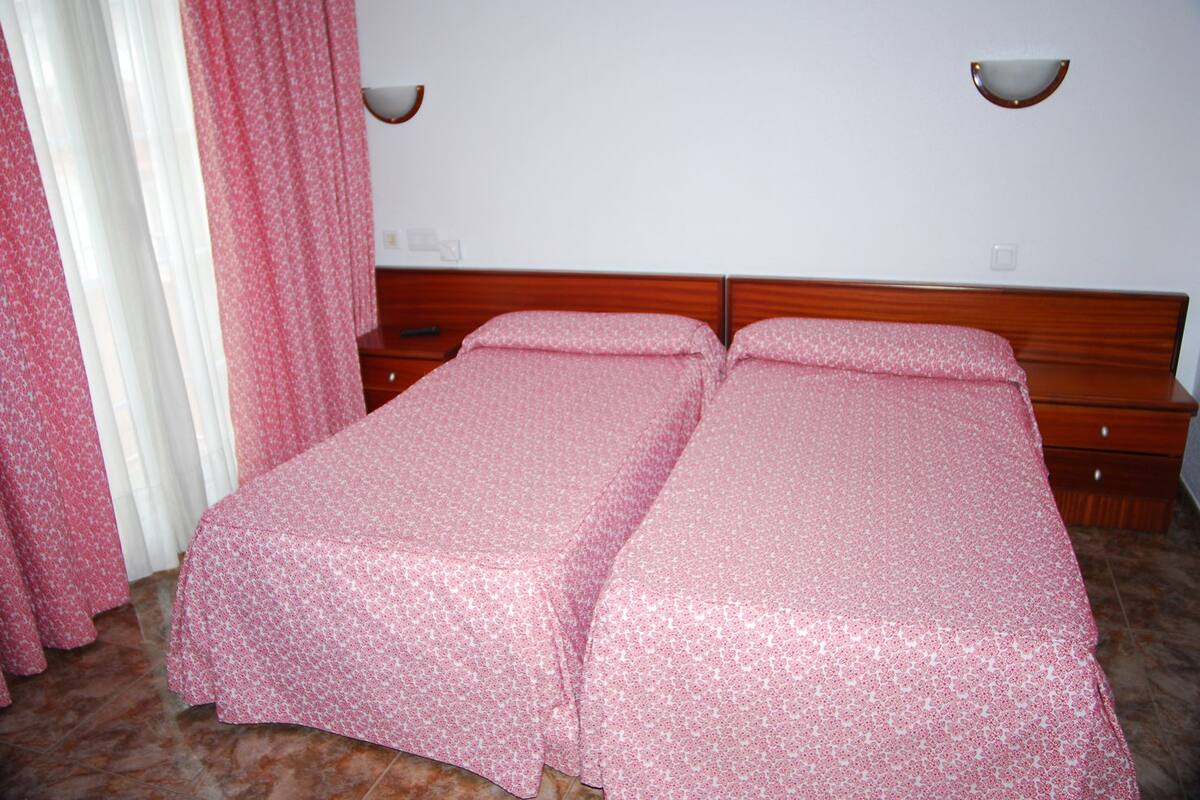 A double bed with a floral bedspread, a wooden headboard, a nightstand, and a wall-mounted lamp.