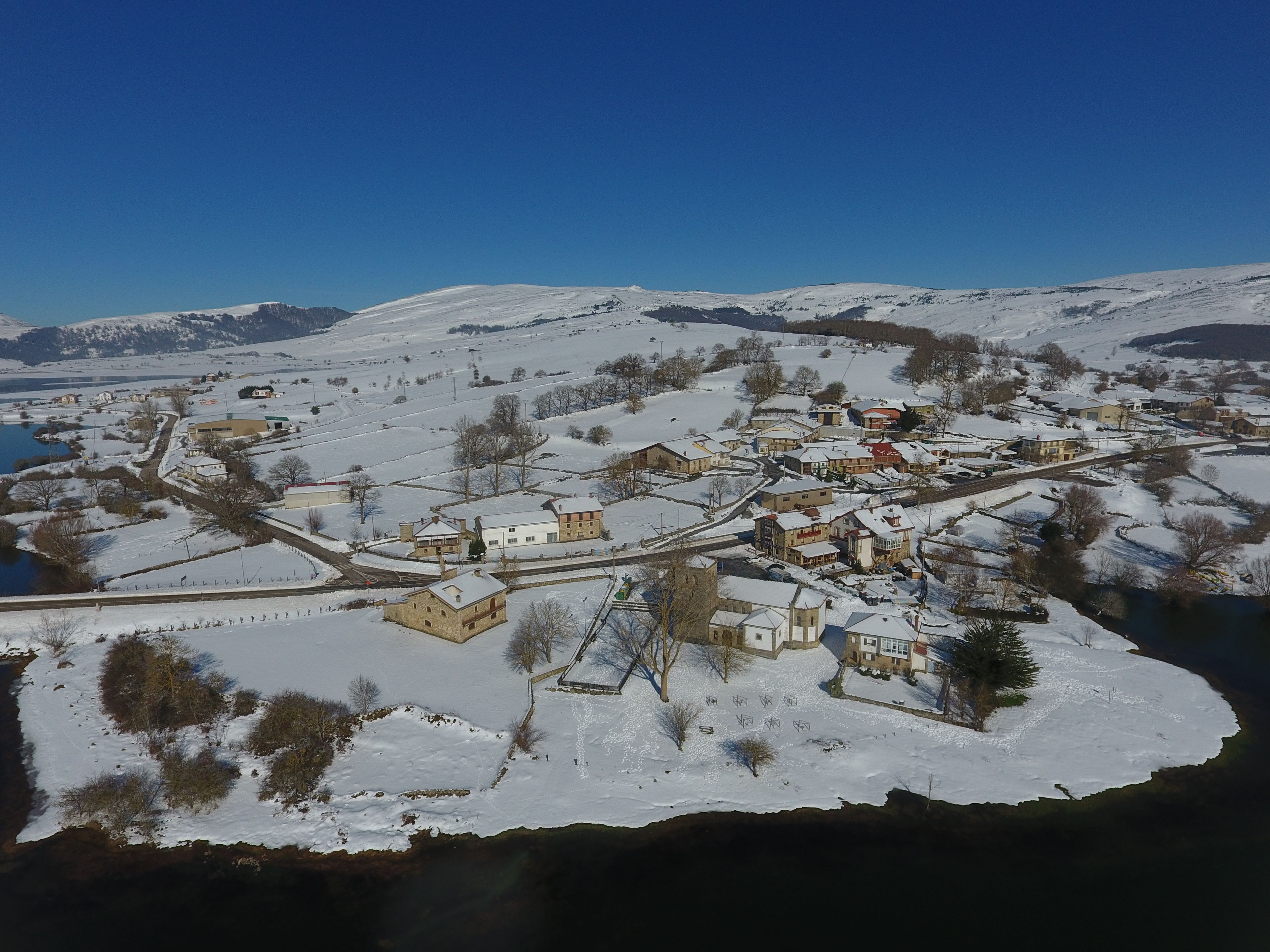 Un pueblo cubierto de nieve con edificios, un río y montañas al fondo.
