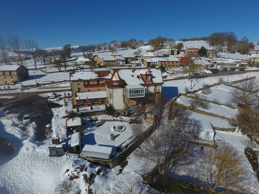 Un pueblo cubierto de nieve con edificios tradicionales, una plaza central con una fuente y un cielo azul despejado.