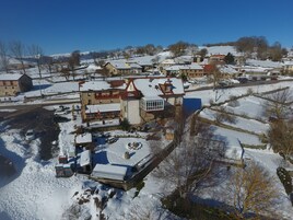 Uma aldeia coberta de neve com edifícios tradicionais, uma praça central com uma fonte e um céu azul límpido.