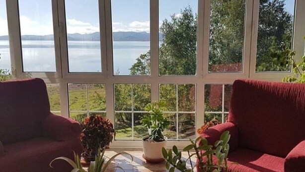 A conservatory with a view of a lake and mountains, featuring two red sofas and potted plants. - Pensión El Carloto (Campoo de Yuso)