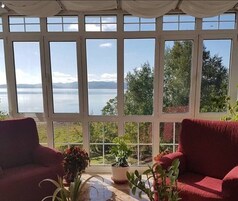 Uma estufa com vista para um lago e montanhas, com dois sofás vermelhos e plantas em vasos.