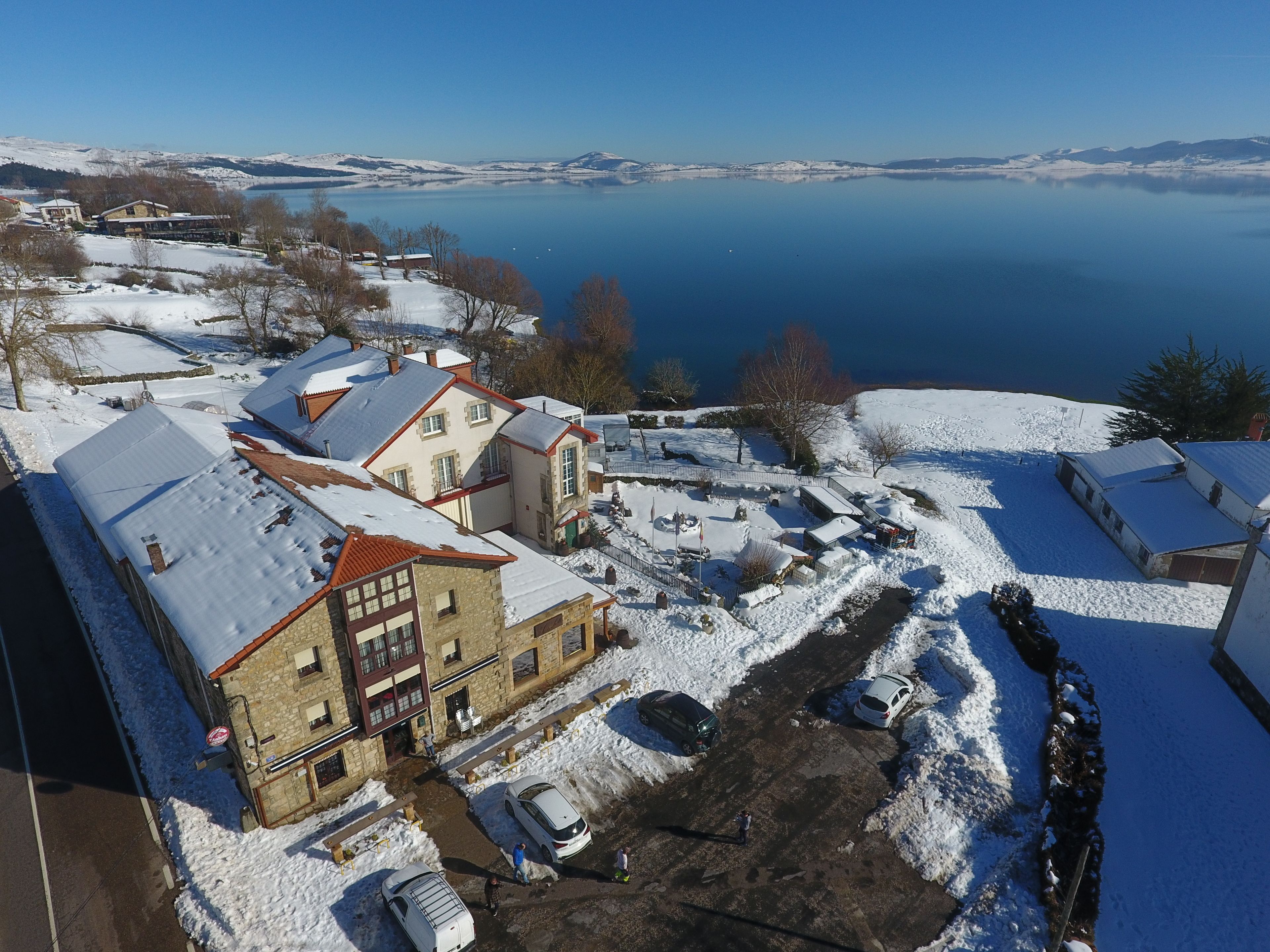 A snow-covered village with buildings, a lake, and a clear sky.