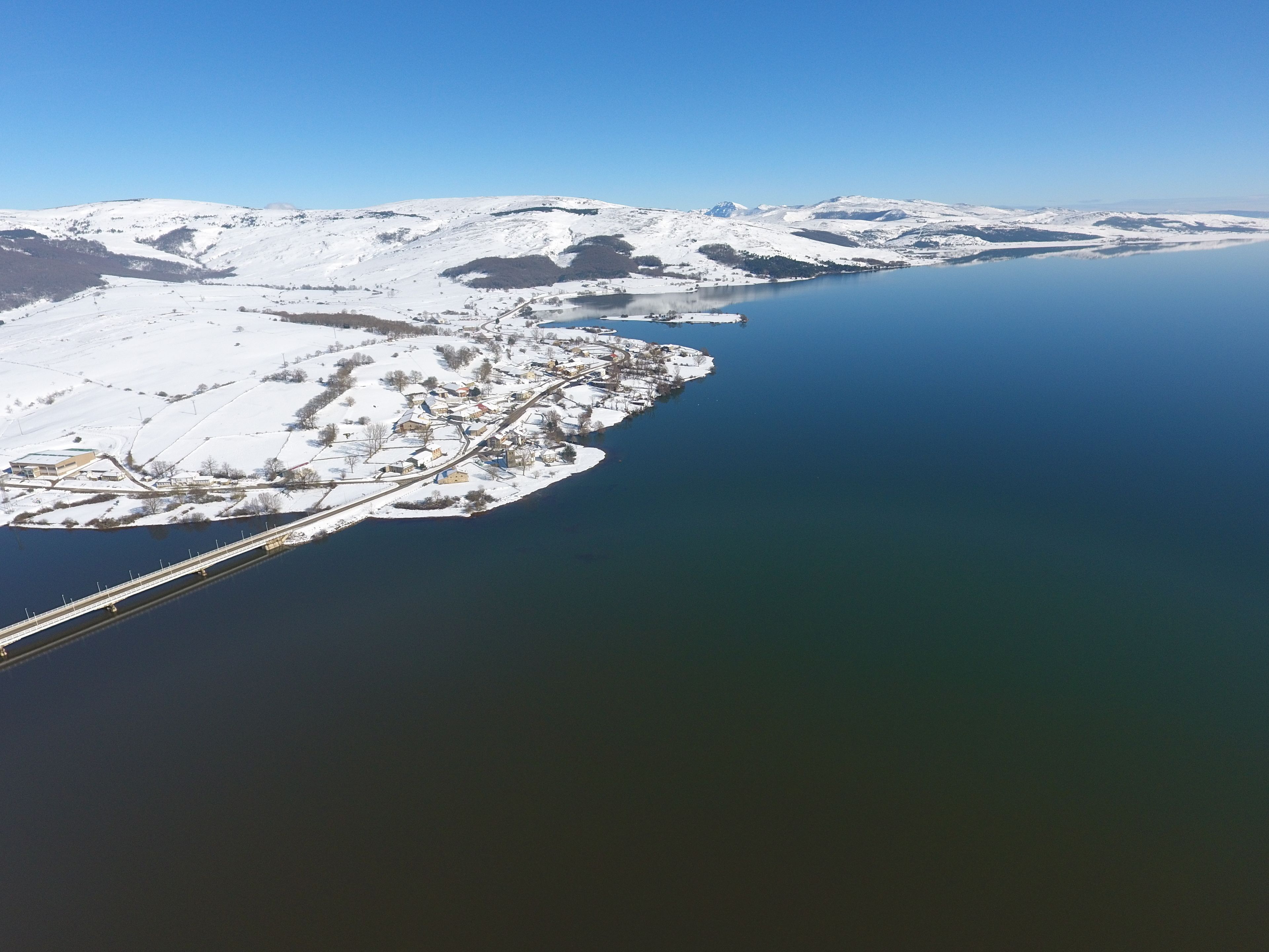 Paisaje nevado con un puente y un lago tranquilo.