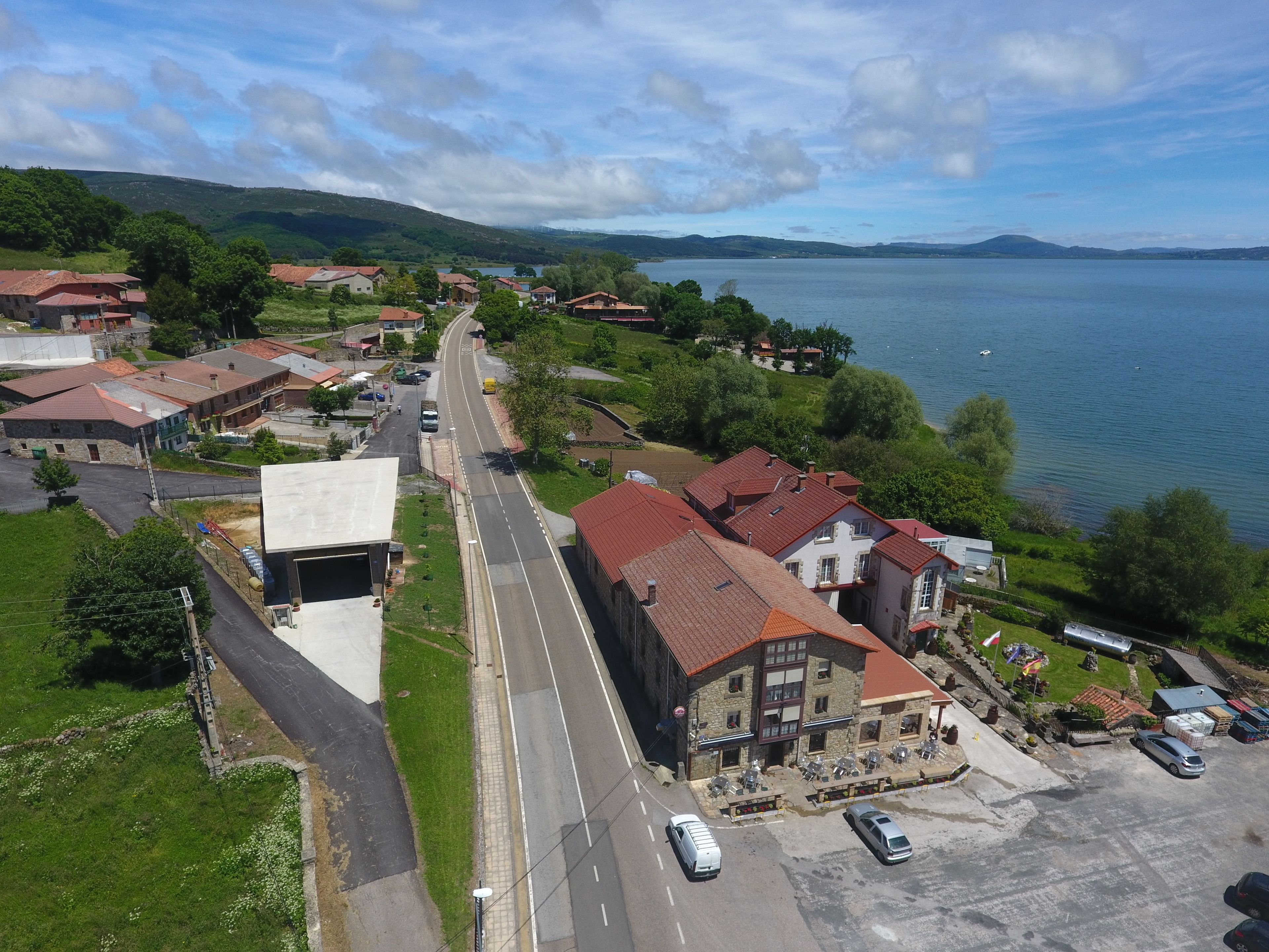 Vista aérea de un pueblo junto al lago, con una calle principal, edificios con tejados rojos y un estacionamiento con coches.