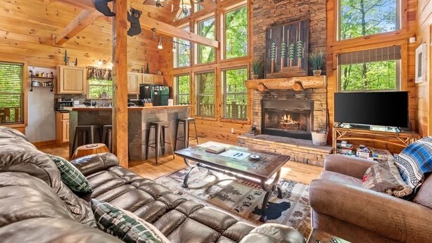 A log cabin interior with a fireplace, wooden walls, a sofa, and a dining area.
