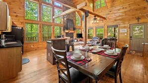 A wooden cabin interior with a dining area, kitchen, and large windows.