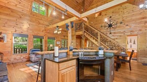 A wooden cabin interior with a kitchen, dining area, and a staircase.