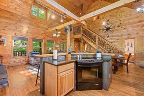 Interior de una cabaña de madera con cocina, comedor y una escalera.