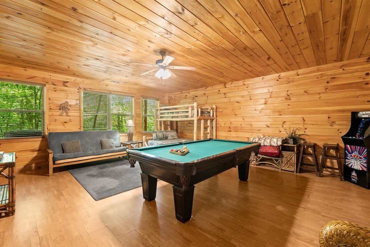 A wooden cabin interior with a pool table, sofa, and arcade game.