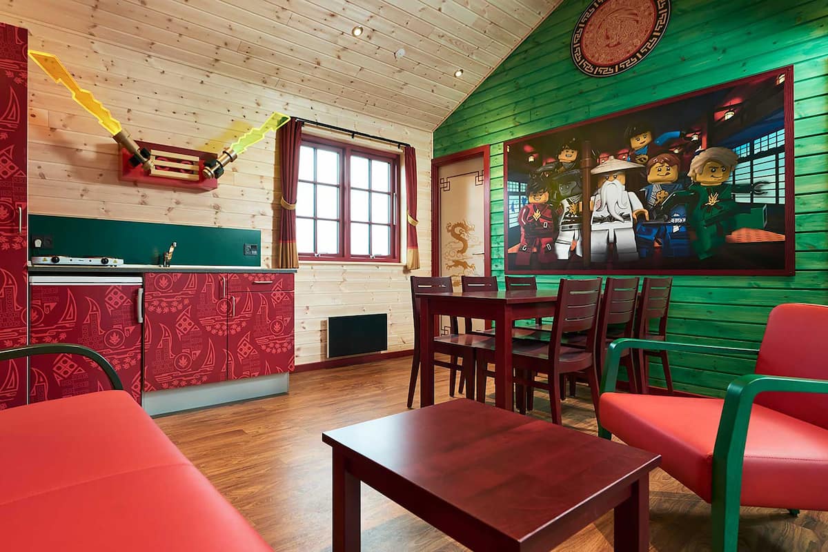 Um quarto acolhedor com teto de madeira, parede com padrão vermelho, parede verde com um mural, uma mesa de jantar com cadeiras e um sofá vermelho.