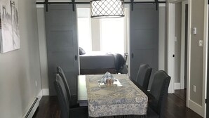 A dining area with a table set for four, a hanging light fixture, and a view through a sliding door to a living space. - Oceanfront oasis located in historical Annapolis Royal.  (Annapolis Royal)