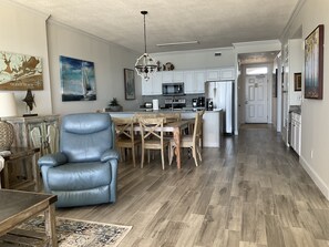 Amplia sala de estar con un sillón de cuero azul, una mesa de comedor de madera y una cocina al fondo.
