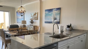 A modern kitchen with a large island, stainless steel appliances, and a dining area with wooden chairs. - Simply Irresistible 2 *Gulf Front View*Make A Reservation For Fun At The Beach! (Orange Beach)