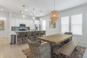 Una cocina moderna con armarios blancos, una isla central y un comedor con mesa de madera y sillas de mimbre.