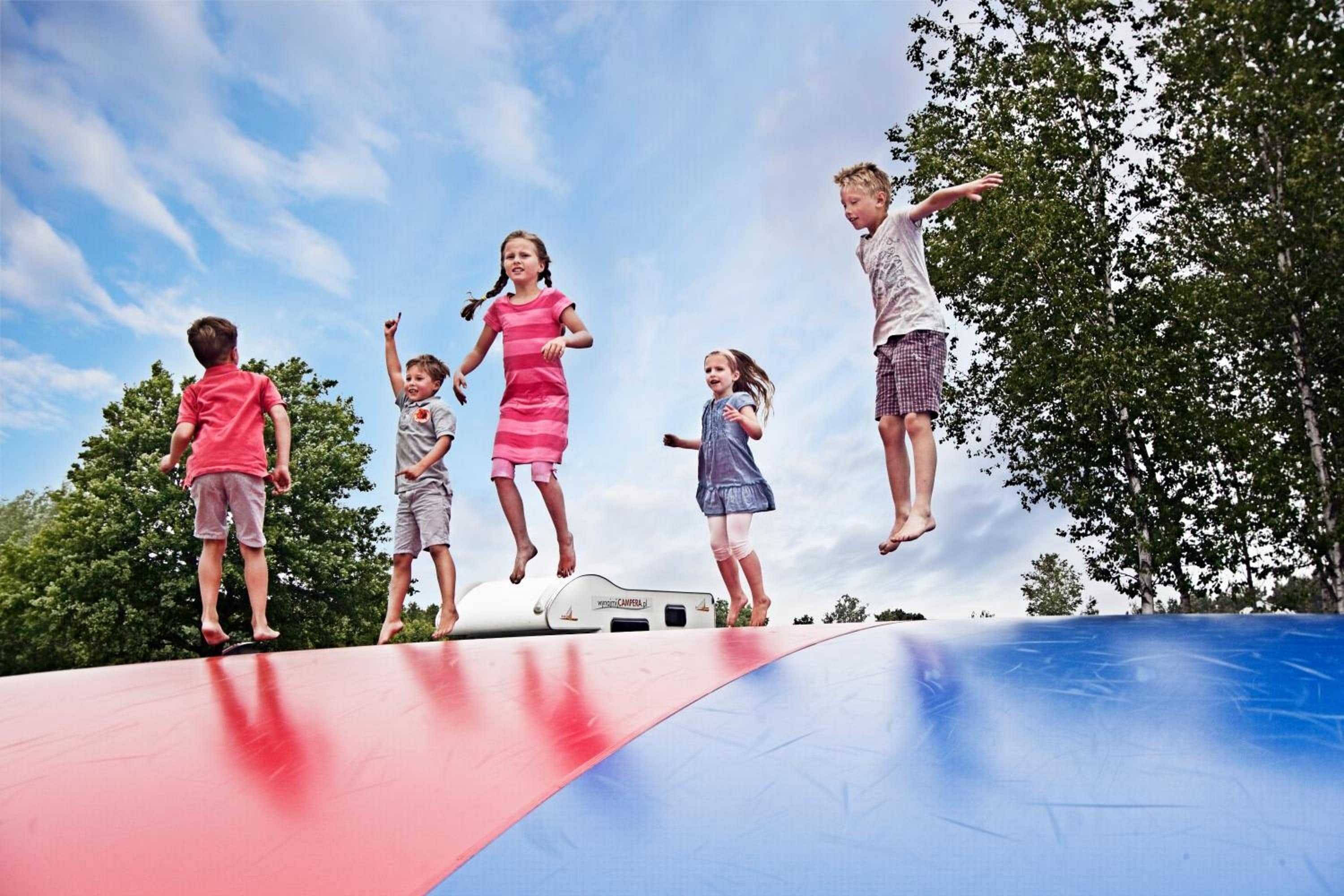 Children jumping on a trampoline with a clear sky and trees in the background.