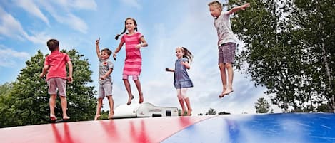 Children jumping on a trampoline with a clear sky and trees in the background.
