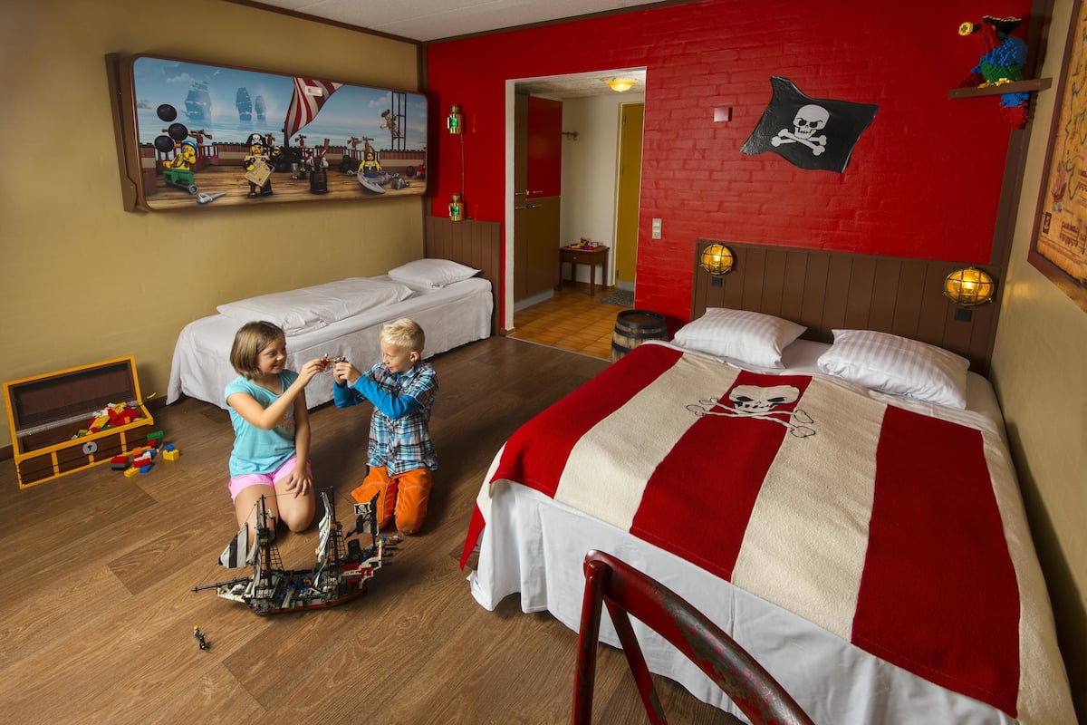 A room with a large bed, two smaller beds, wooden flooring, a toy ship, and a pirate-themed wall.
