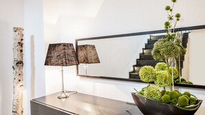 A modern interior with a dark wood console, a reflective mirror, a birch tree, and a decorative bowl with green spheres. - Hotel Concordia (Euskirchen)