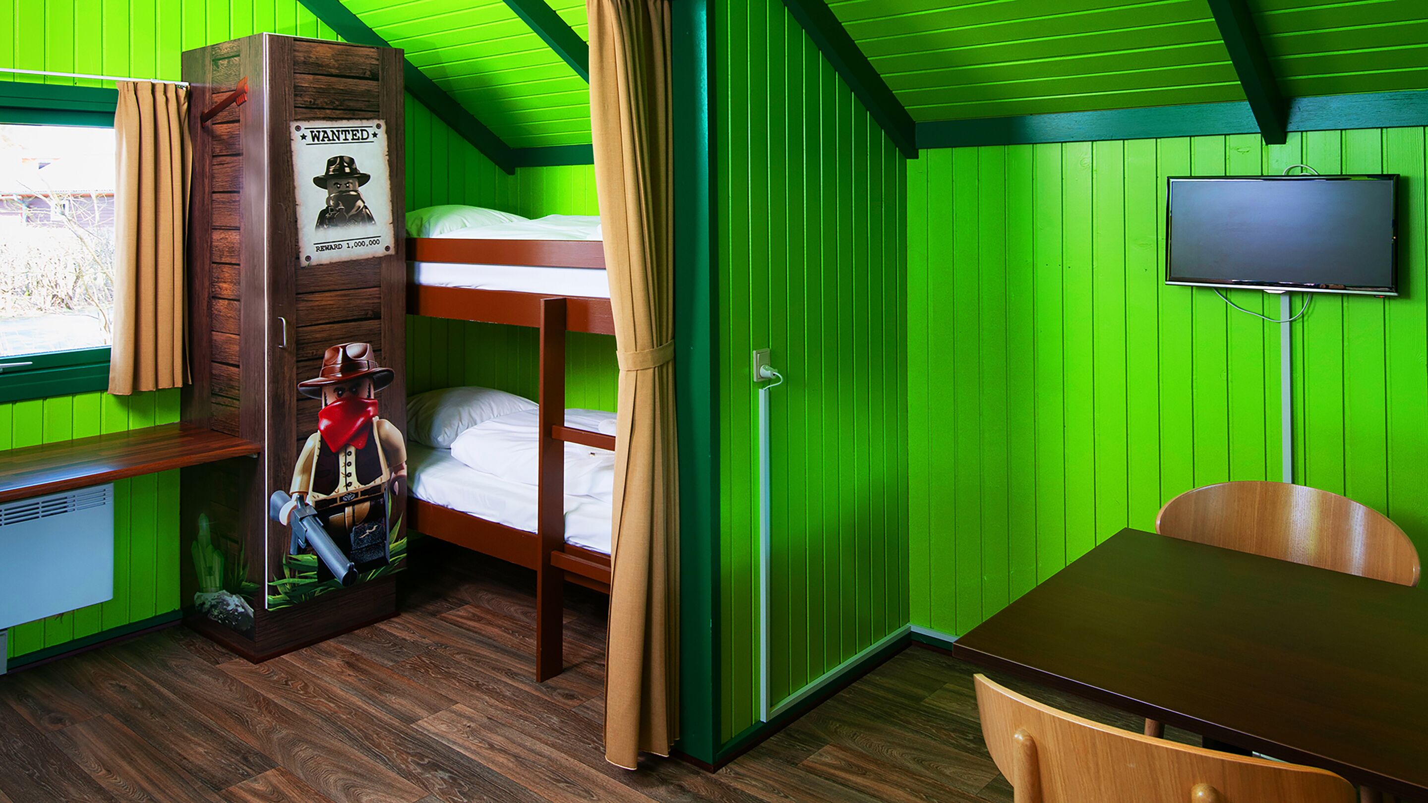 A room with bunk beds, a wooden desk, a television, and a window with curtains.