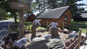 A raccoon-themed exhibit with a wooden sign, a fenced area, and a small building in the background.