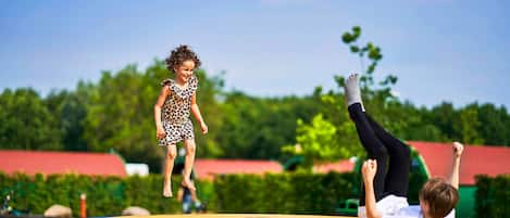 A child jumping on a trampoline with a playground in the background.