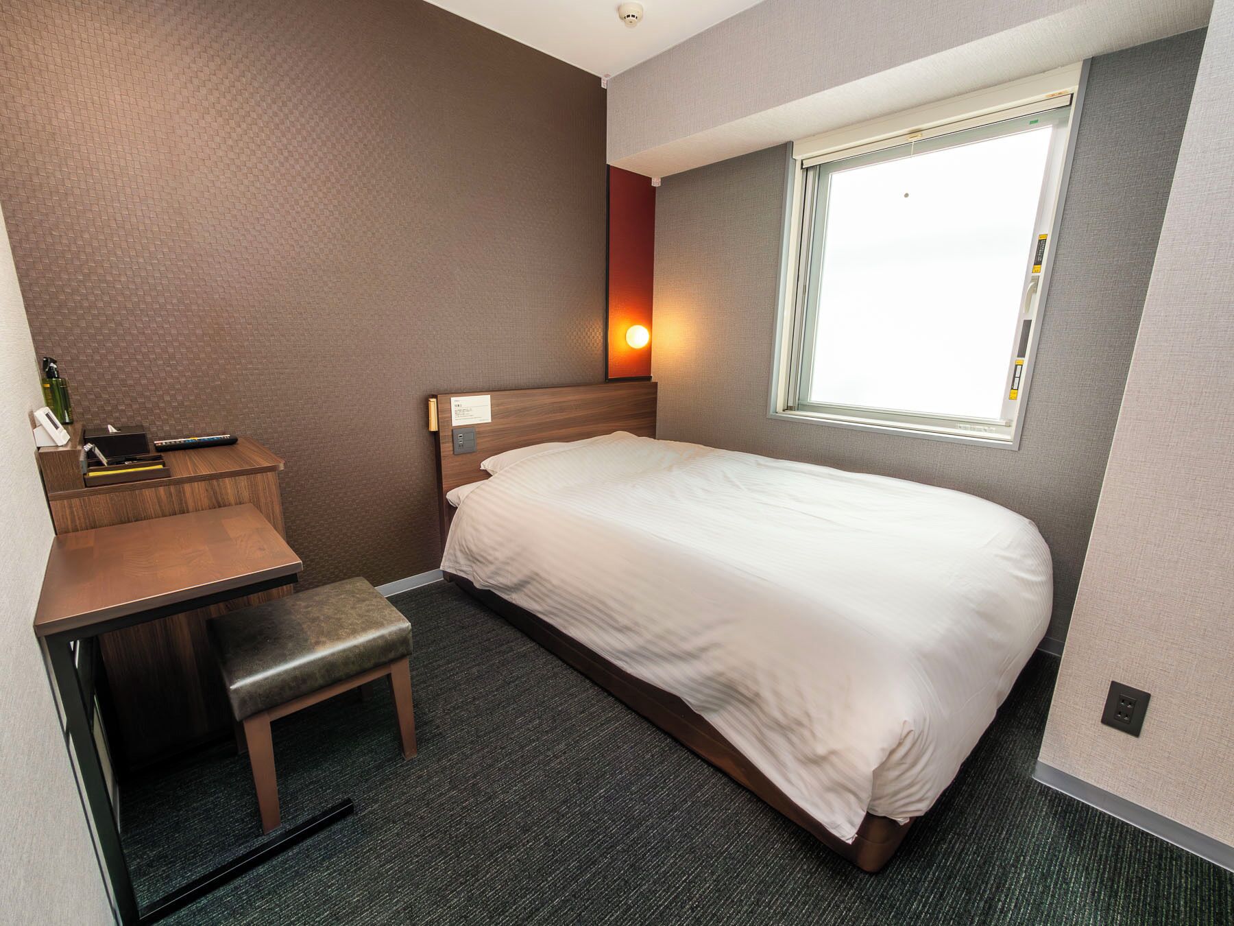 A hotel room with a bed, a desk, a chair, and a window.