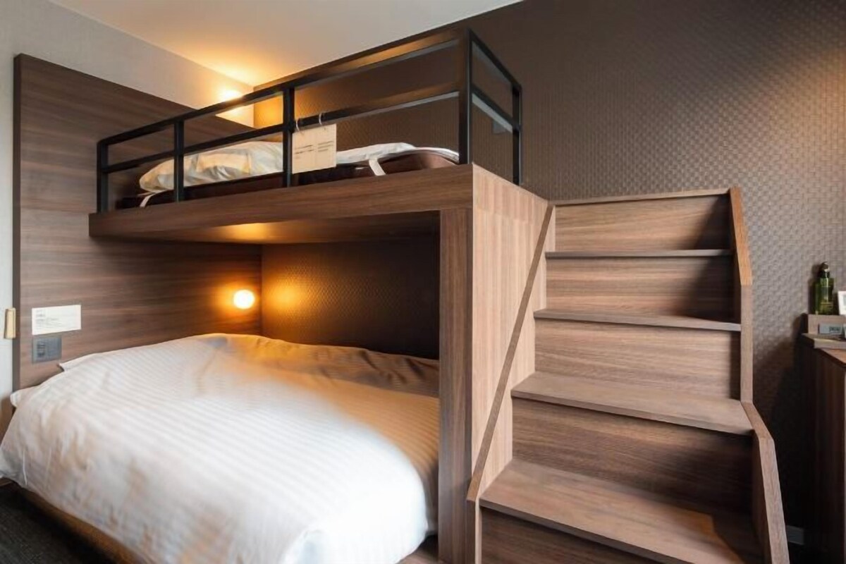 Una cama litera con escalera de madera, una mesita de noche y una lámpara de pared.