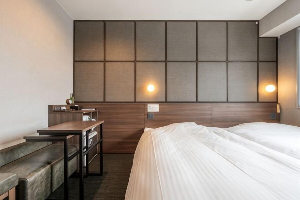 Habitación de hotel con cama, escritorio, silla y lámpara de pared.