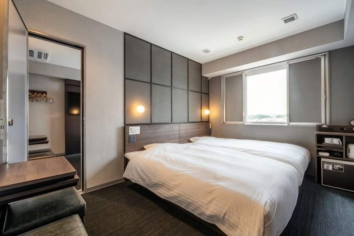 A hotel room with a bed, a desk, a wardrobe, and a window.