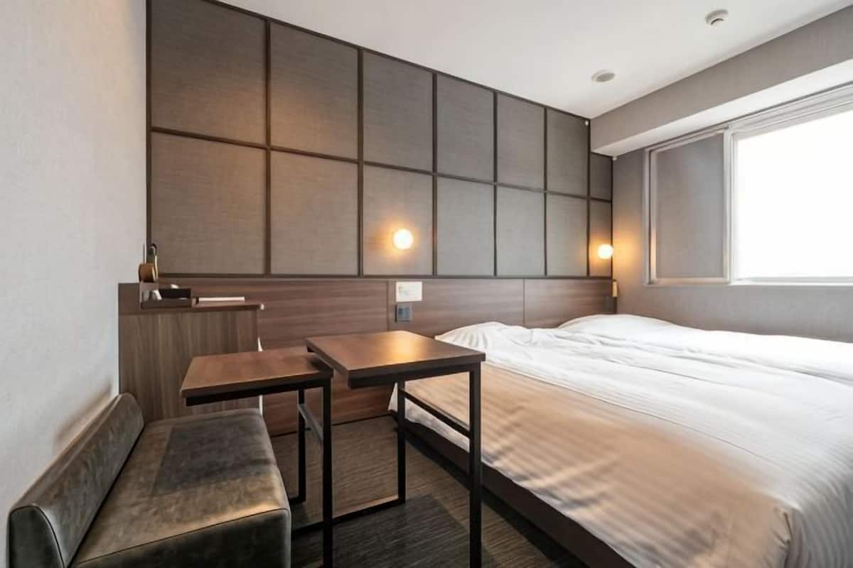 Hotellihuone, jossa on sänky, työpöytä, penkki, seinäpaneeli ja ikkuna.