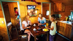 A family dining in a cabin with wooden interiors, a kitchen area, and a dining table with food and drinks. - LEGOLAND Wild West Cabins (Billund)