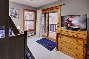 A room with a wooden dresser, a television, a large window with curtains, and a blue rug.