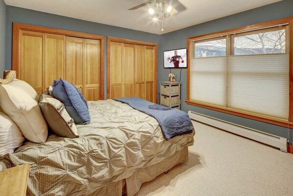 A bedroom with a bed, wooden wardrobe, television, and a window with blinds.