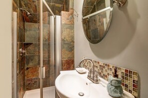 Un bany amb plat de dutxa de vidre, un lavabo blanc i una barra de rajoles mosaic.