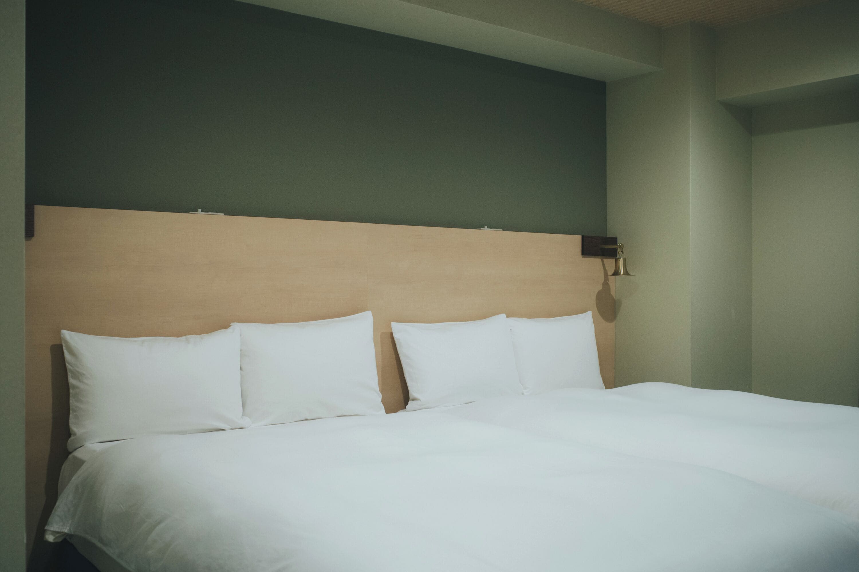A neatly made bed with white linens in a room with a green wall and a wooden headboard.