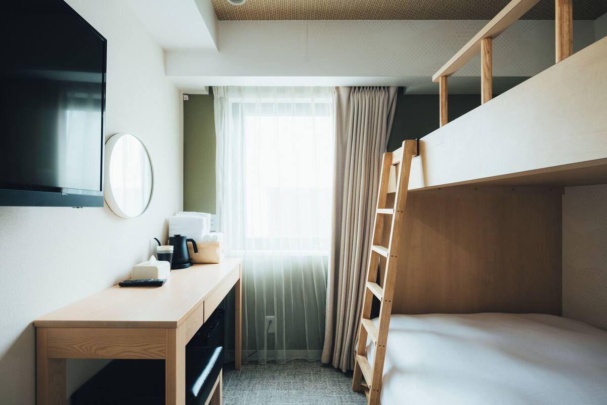 Hotellihuone, jossa on kerrossänky, työpöytä, kahvinkeitin, televisio ja ikkuna, jossa on verhot.