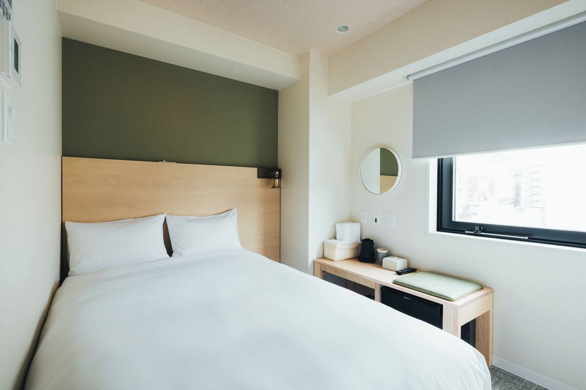 Hotellihuone, jossa on suuri sänky, puinen pääty, yöpöytä lampun kanssa, peili ja ikkuna, josta on näkymä.