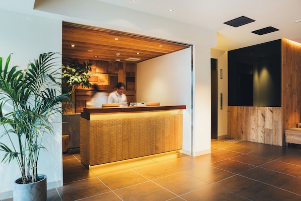 A reception area with a wooden counter, potted plants, and a modern interior design. - Meander Osaka (Osaka)