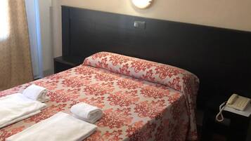 A hotel room with a bed, a nightstand, and a wall-mounted telephone.