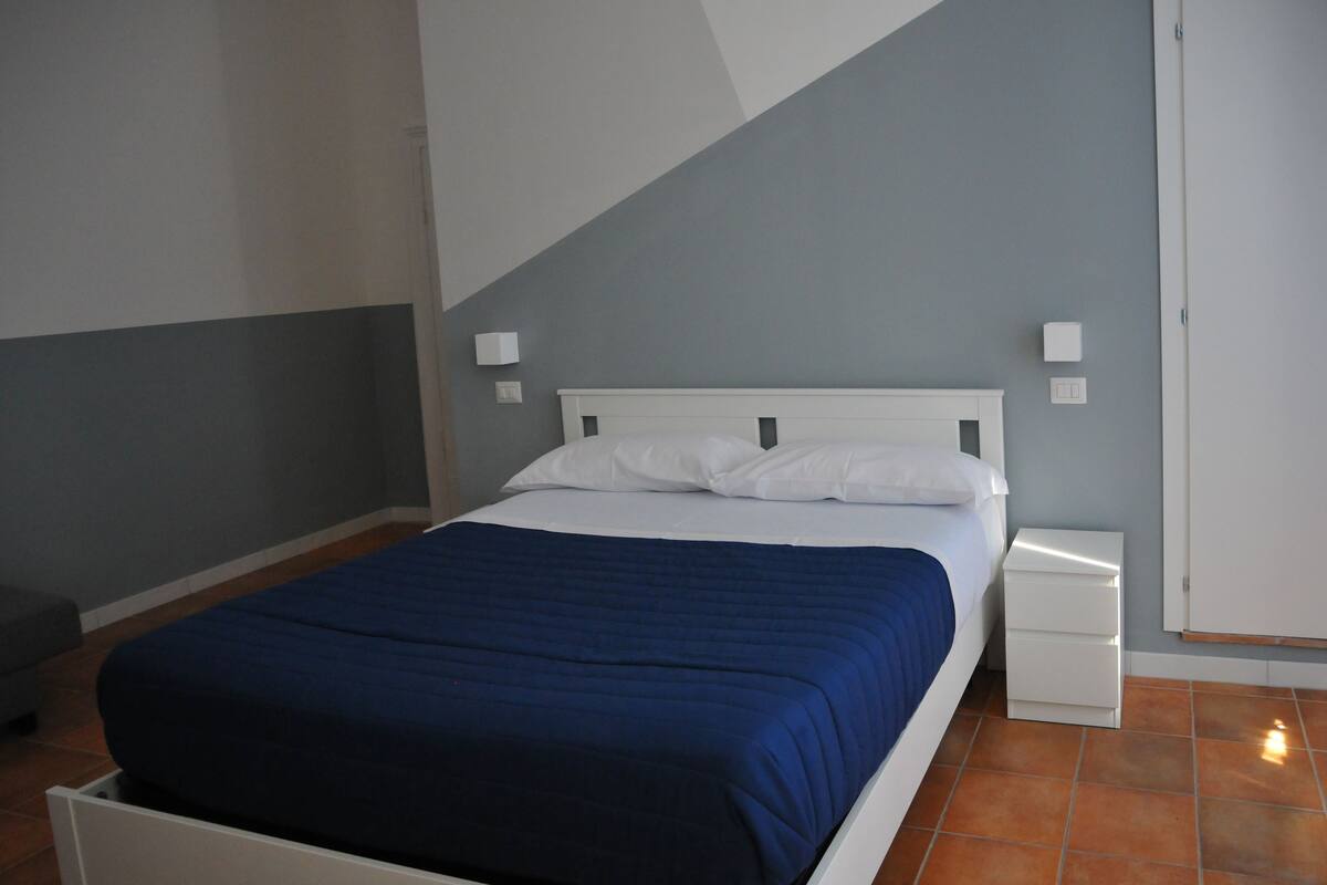 A bedroom with a bed, white nightstands, and a grey wall.
