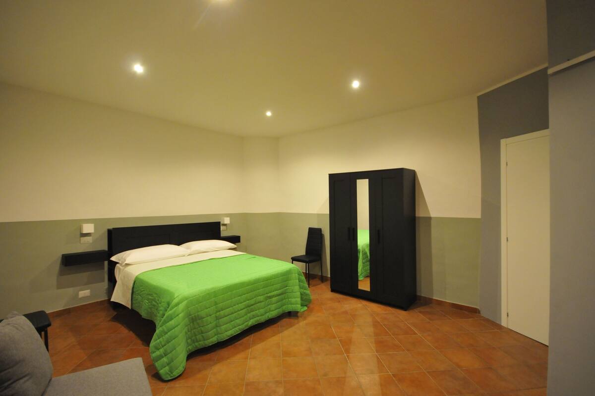 A bedroom with a bed, a chair, a wardrobe, and a door.